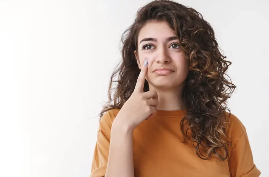 Curly haired woman touching her cheek while wondering how to protect her dallas weather skin through changing seasons