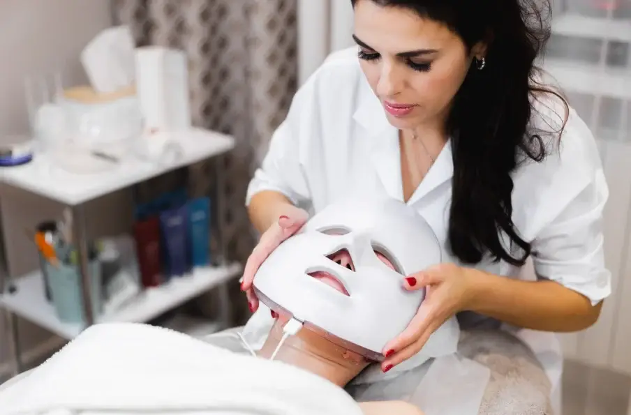 Esthetician placing an LED therapy mask on a client to repair dallas weather skin damage at a facial spa
